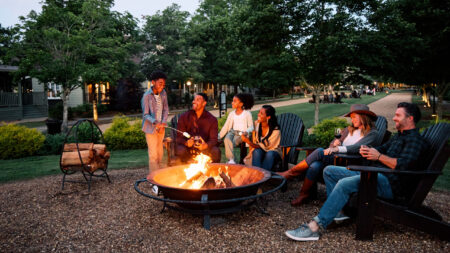 Adults and kids gathered around a firepit at Barnsley Resort roasting marshmallows and drinking wine