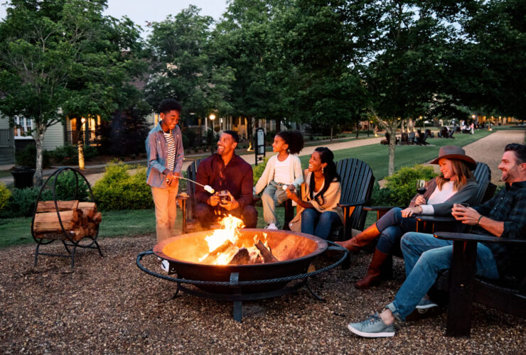 Adults and kids gathered around a firepit at Barnsley Resort roasting marshmallows and drinking wine