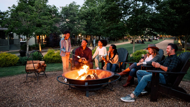 Adults and kids gathered around a firepit at Barnsley Resort roasting marshmallows and drinking wine