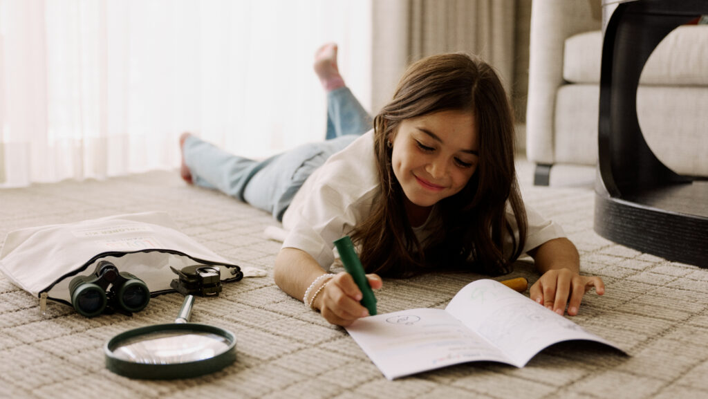 A girl lying on a carpet with a science kit and activity book